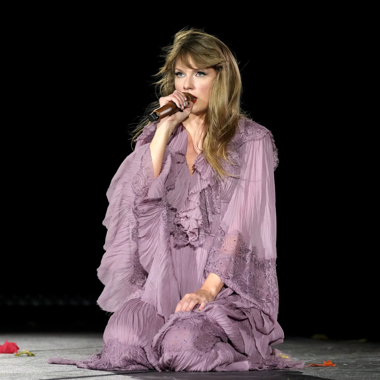 Taylor Swift on stage during the 'Eras Tour,' dressed in a flowing white gown with intricate embroidery, reflecting the dreamy and introspective style of her 'Folklore' album era.