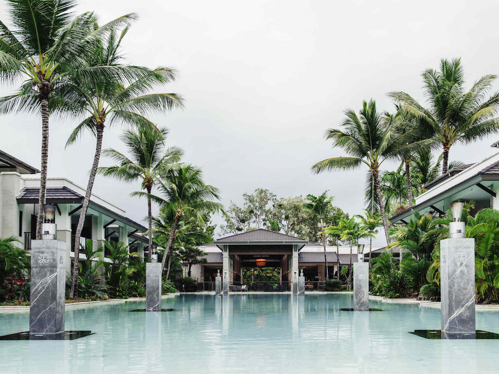 A luxurious pool at Pullman Port Douglas resort, surrounded by tall palm trees and elegant architecture, offering a tropical and relaxing atmosphere.